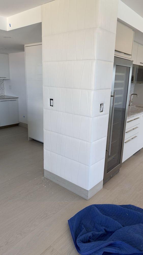 Custom white upholstered wall panels wrapping a kitchen column
